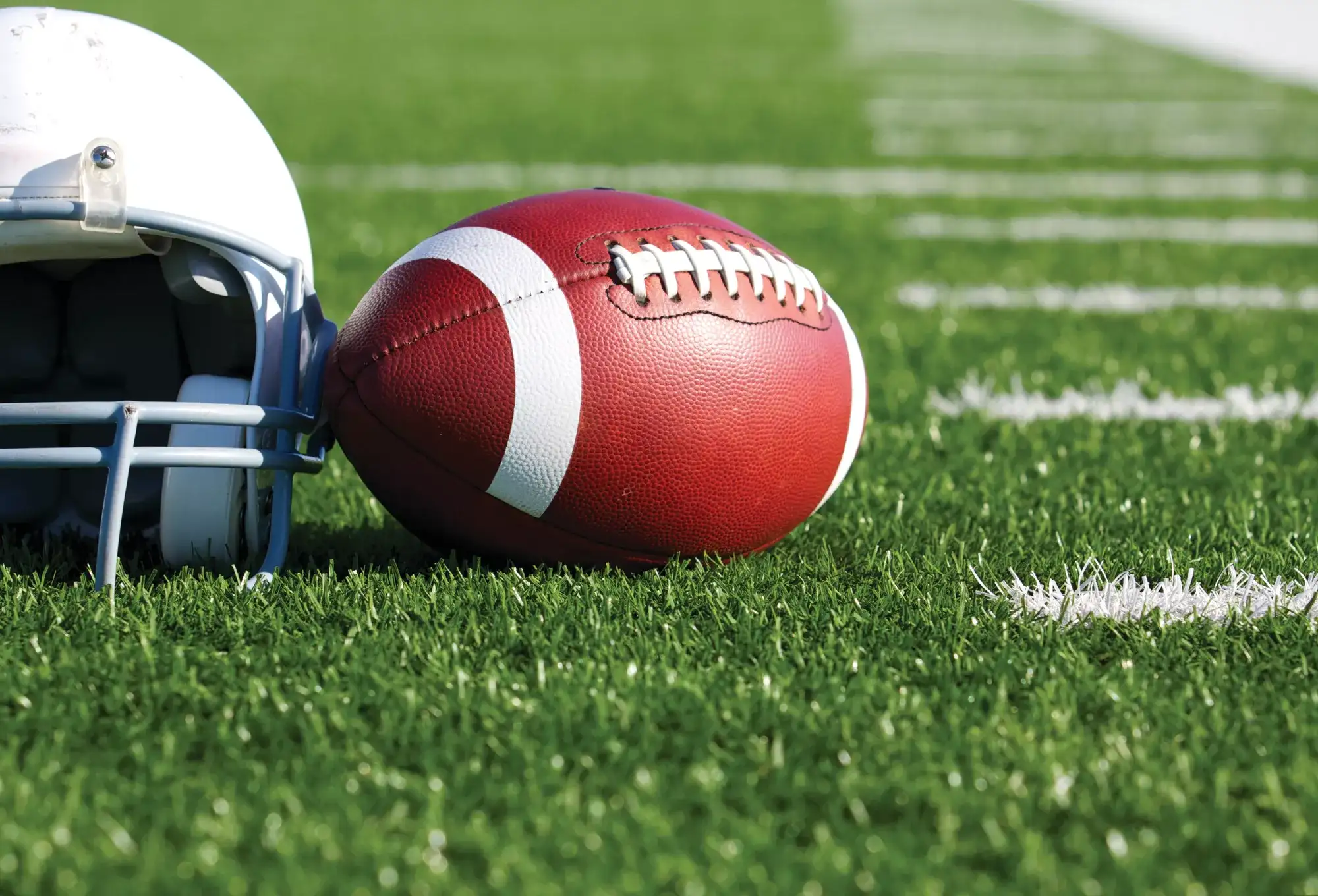Football next to a white helmet on a green grass football field