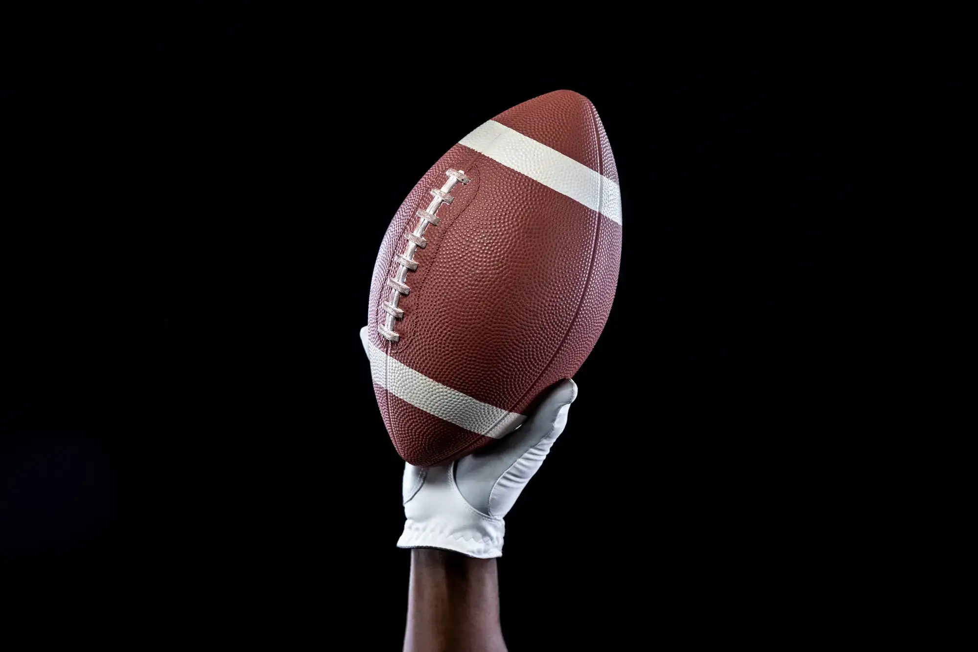 White-gloved hand holding an upright American football against a solid black background