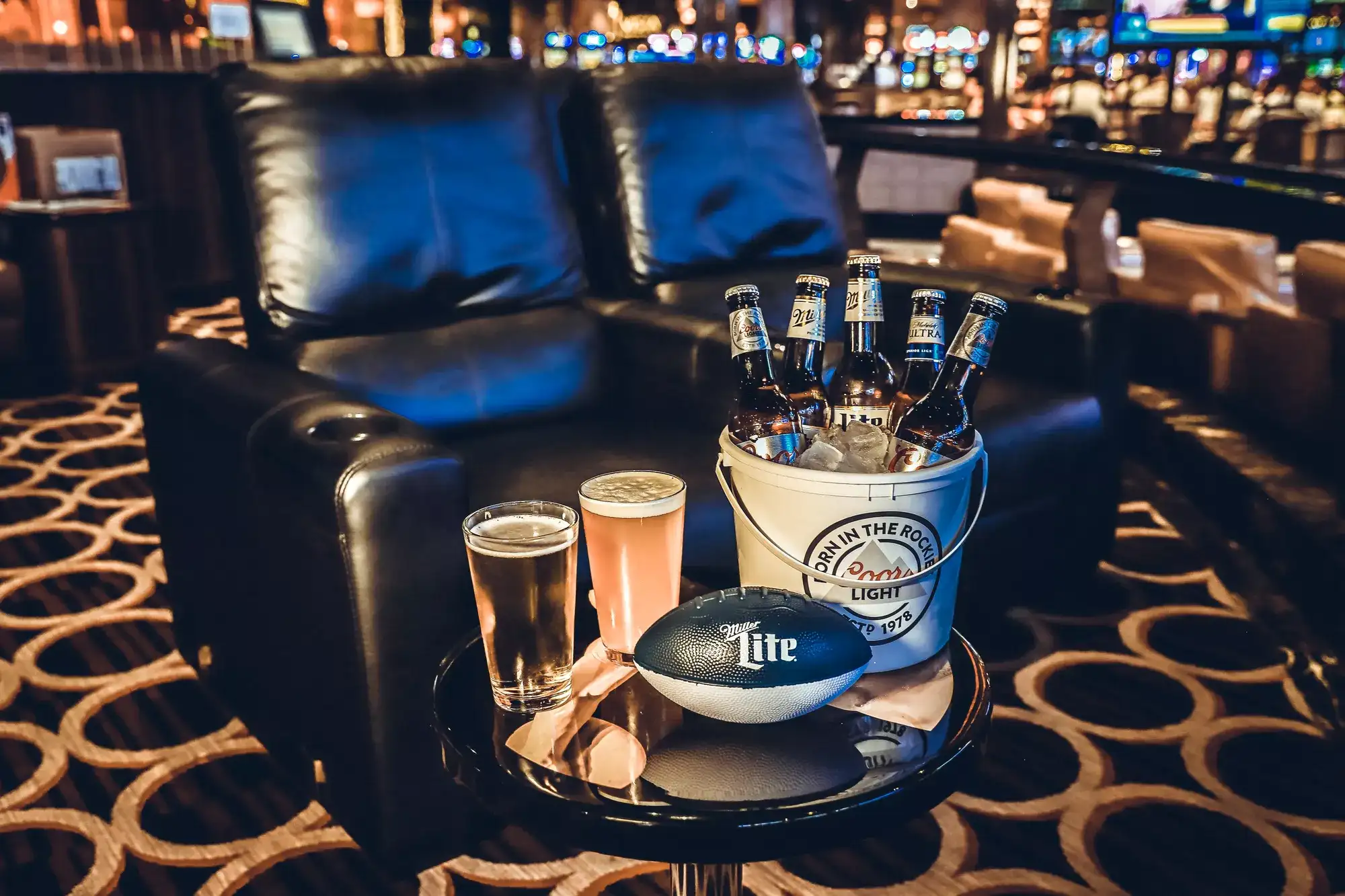 Lounge chairs, drinks, and a football in a Las Vegas sportsbook with big game screens in the background.