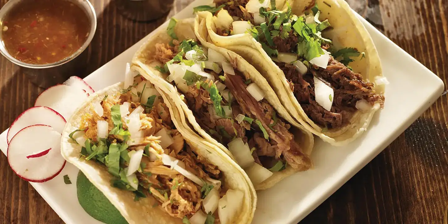 Three tacos on a plate with a side of salsa.