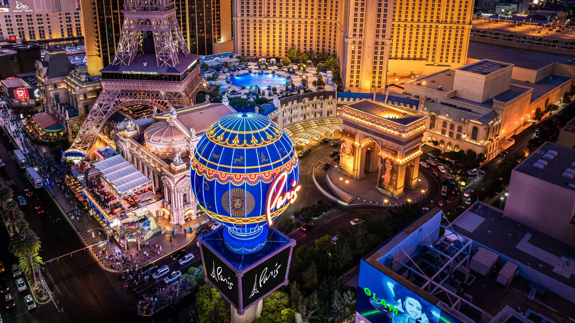 Aerial nighttime view of Paris Las Vegas featuring the illuminated balloon sign, Arc de Triomphe, and Eiffel Tower replica