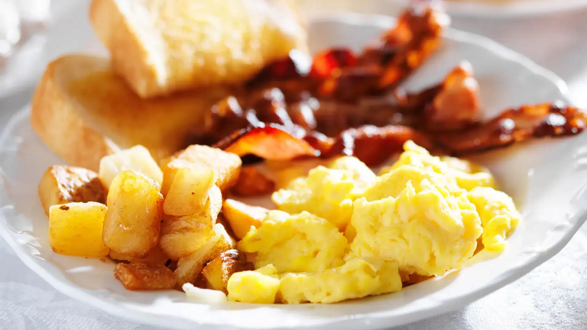 Plate of eggs, potatoes and bacon with a side of toast.