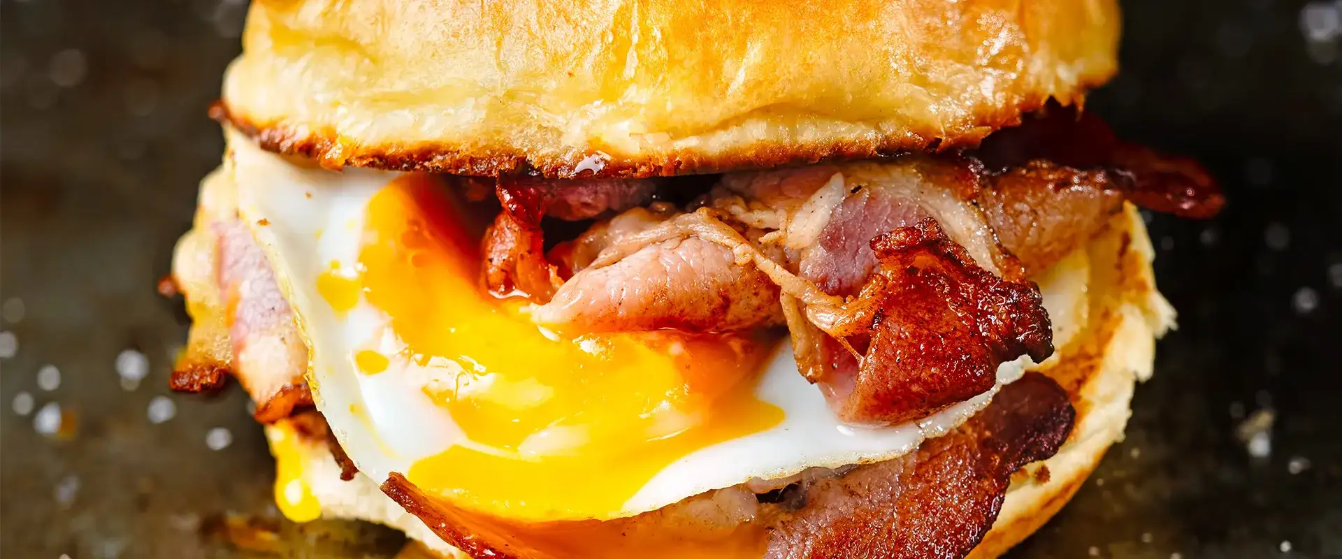 Close-up of a breakfast sandwich with eggs, ham, and bacon.