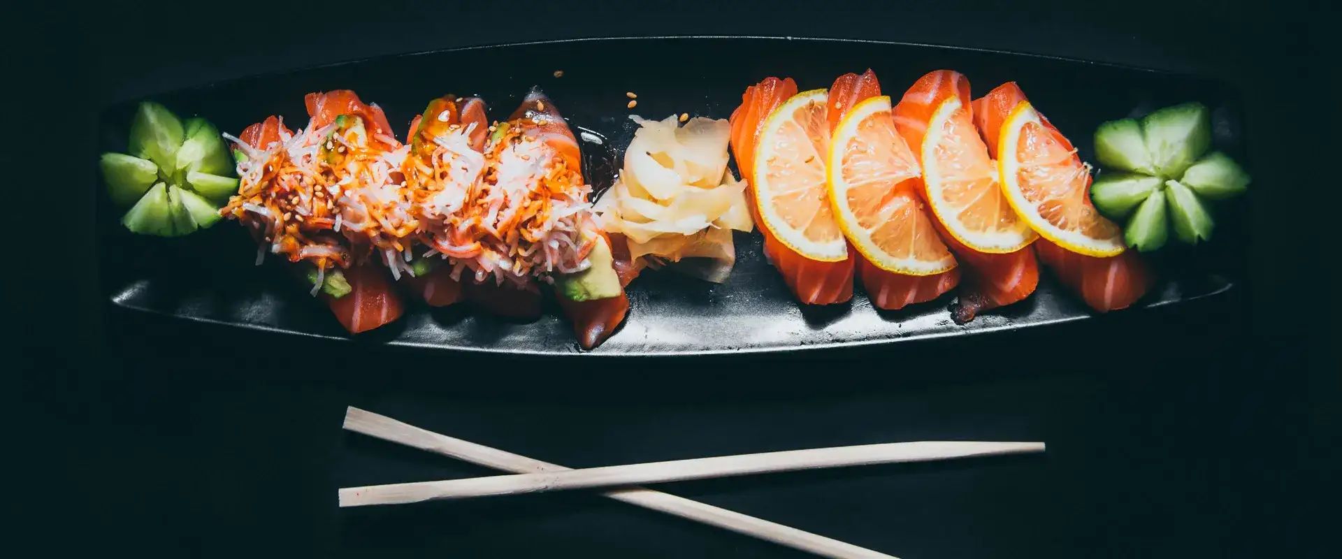 Sushi on a plate with fresh ginger and cucumber flowers.