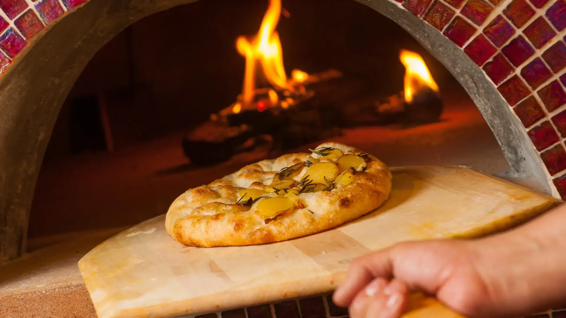 Pizza on wooden paddle coming out of wood fired brick oven.