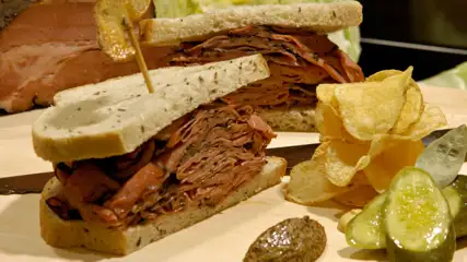 Meat sandwich with a side of chips and pickles.