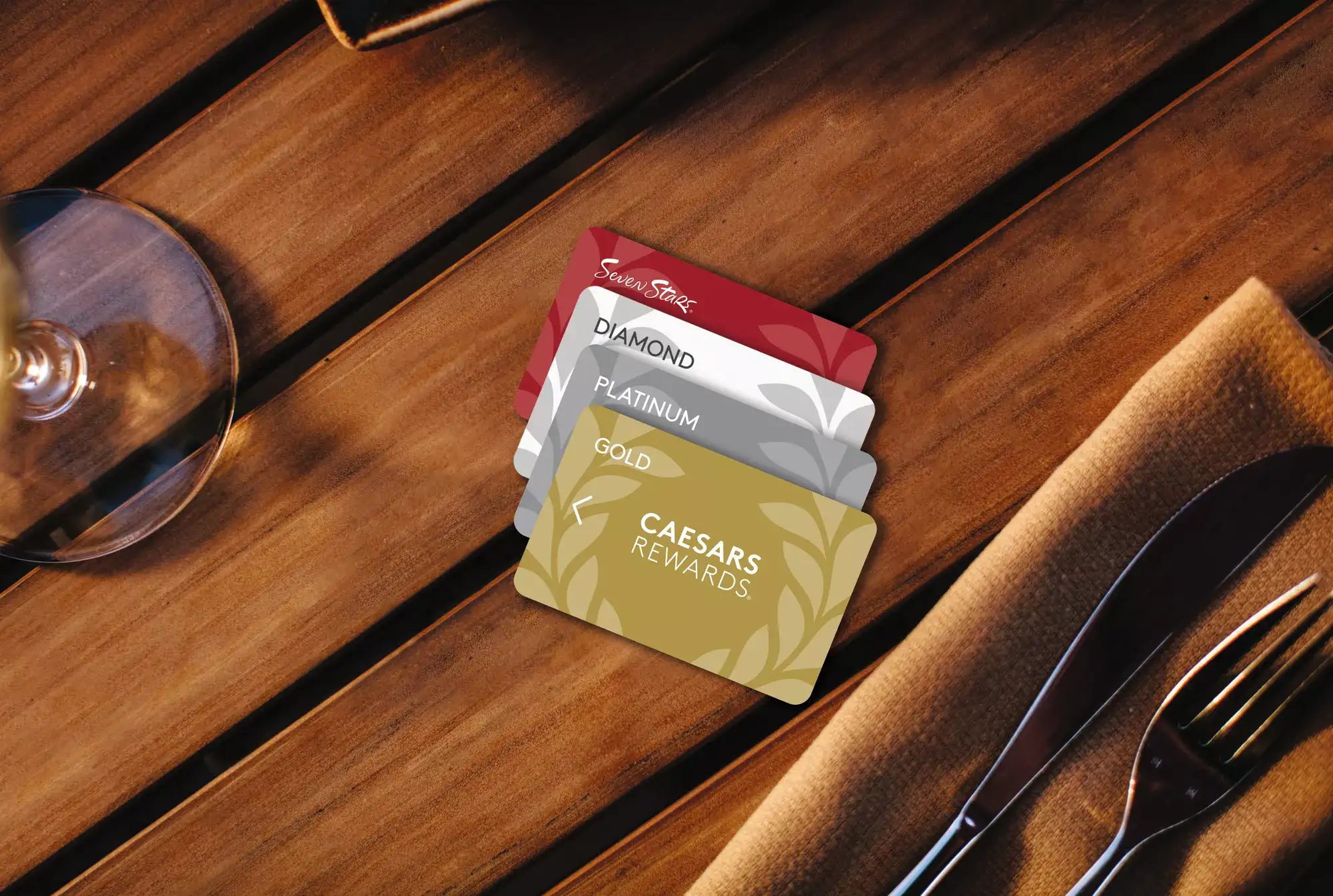Caesars Rewards membership cards showing Gold, Platinum, Diamond, and Seven Stars tiers beside dining utensils