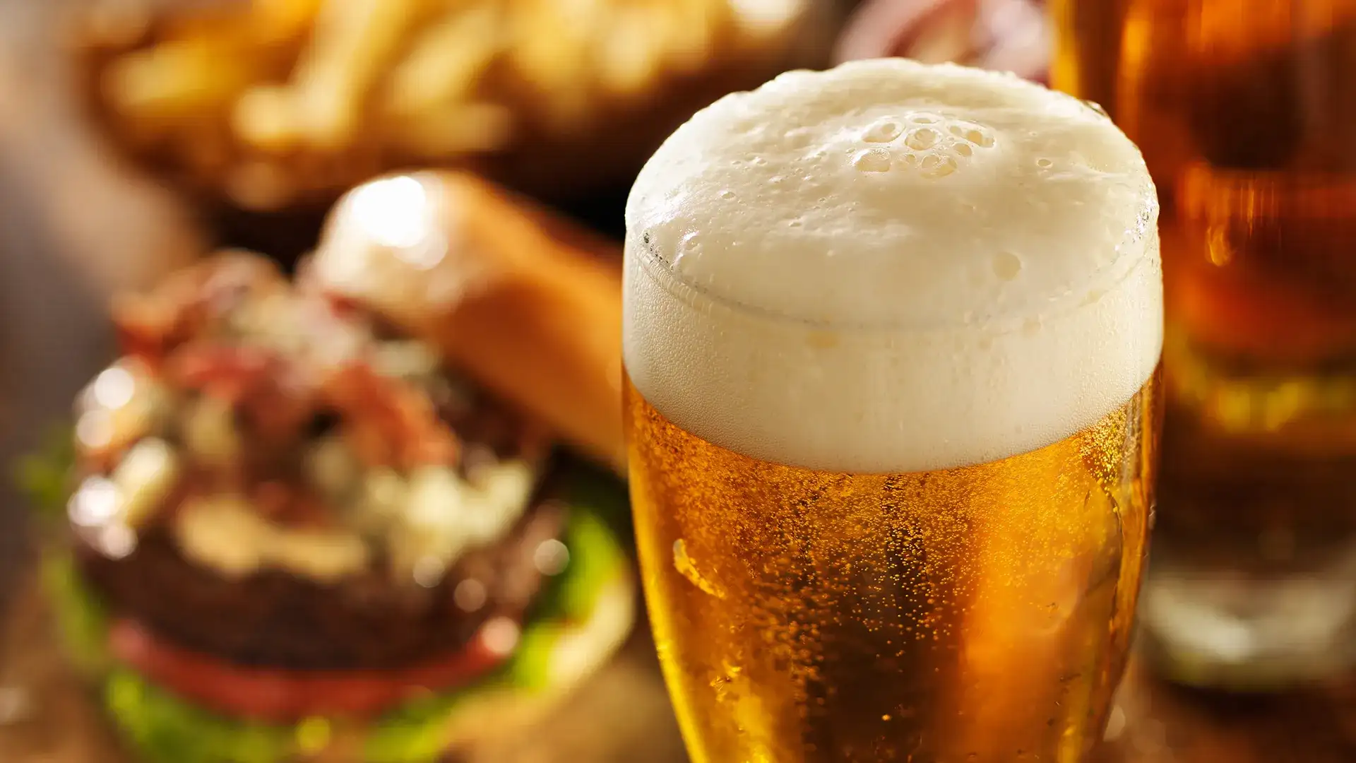 Glass of beer with burger in background.