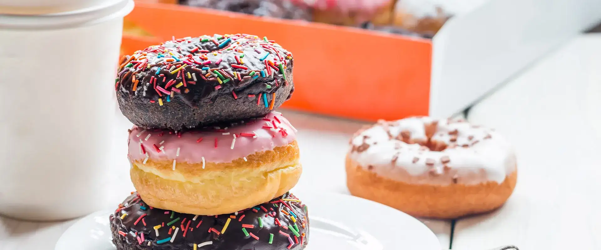 Stack of sprinkled donuts on a plate with a drink to-go and a box of donuts.