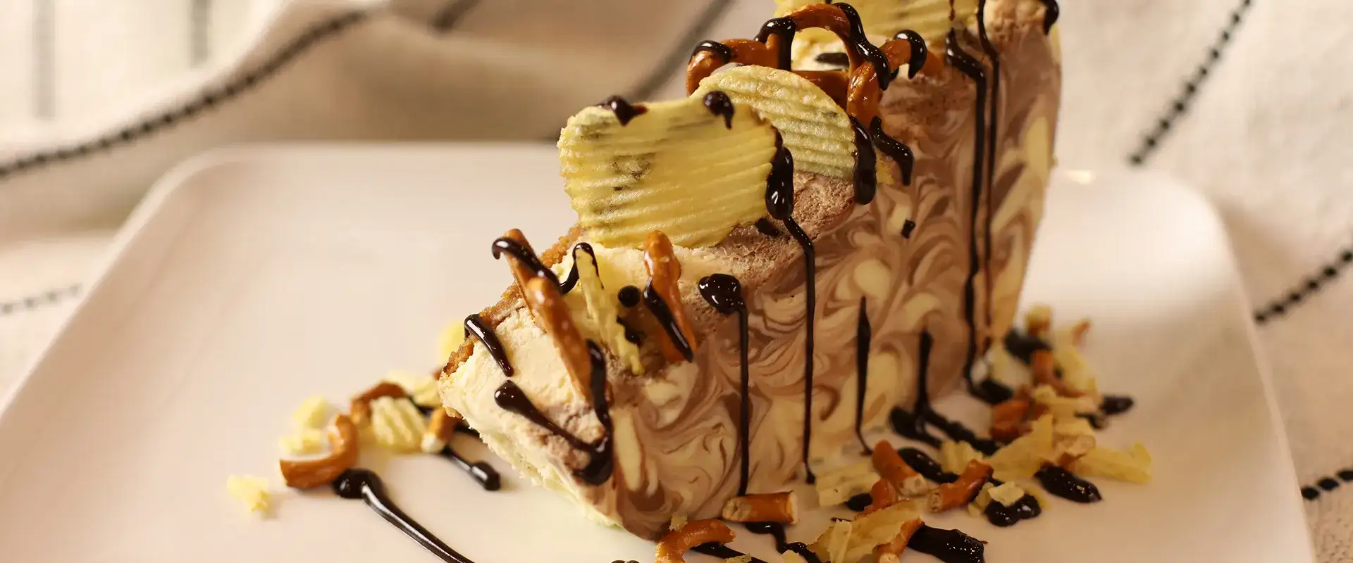 Cheesecake with chocolate drizzle and potato chip topping.