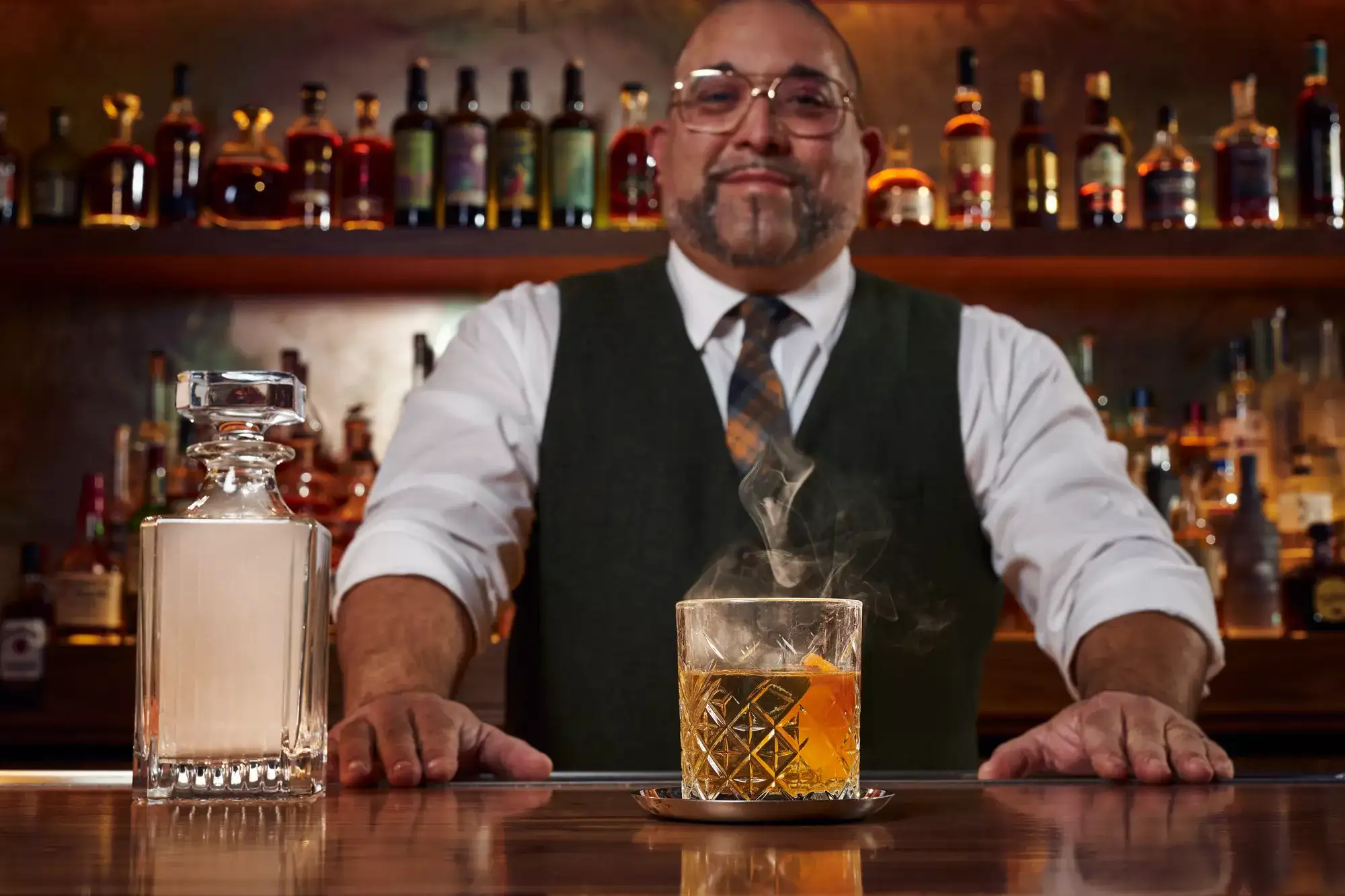 Bartender at The Count Room speakeasy at Flamingo Las Vegas serving a smoky whiskey cocktail beside a crystal decanter and backlit liquor bottles.