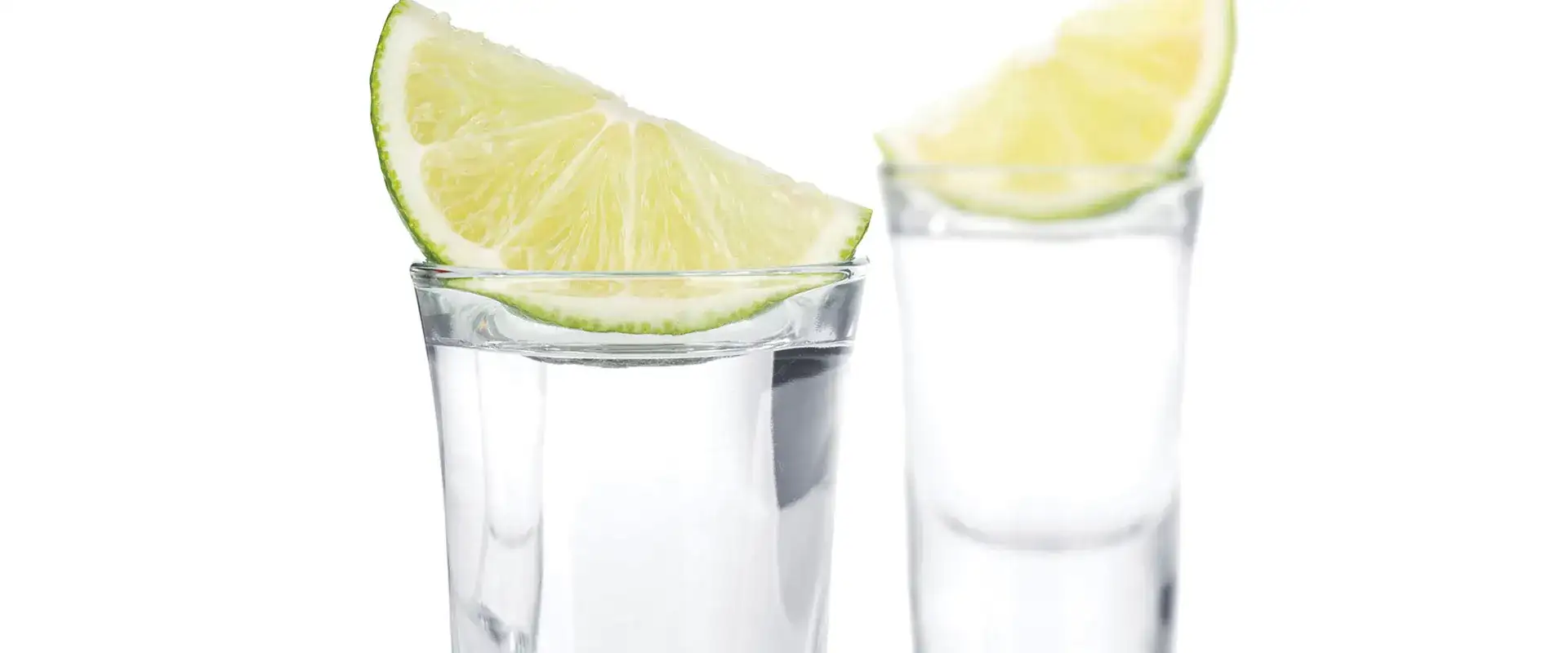 Two tequila shots with lime wedges on top.