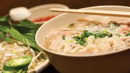 Bowl of Pho with chop sticks with bean sprouts and sliced jalapenos on the side.