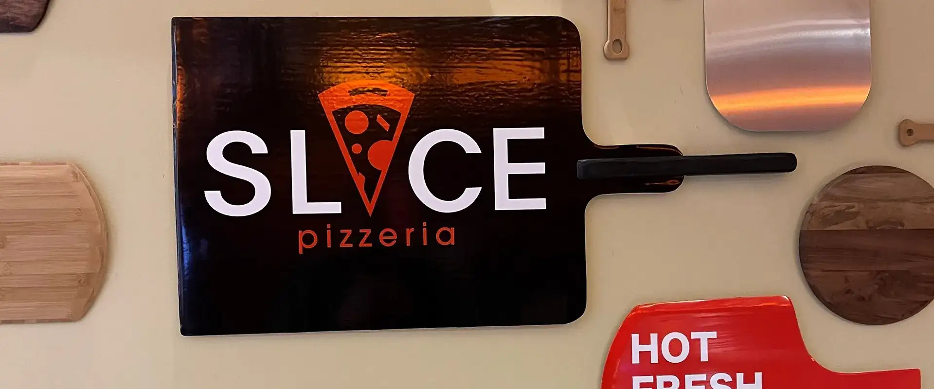 Slice Pizzeria branded peel surrounded by other peels.