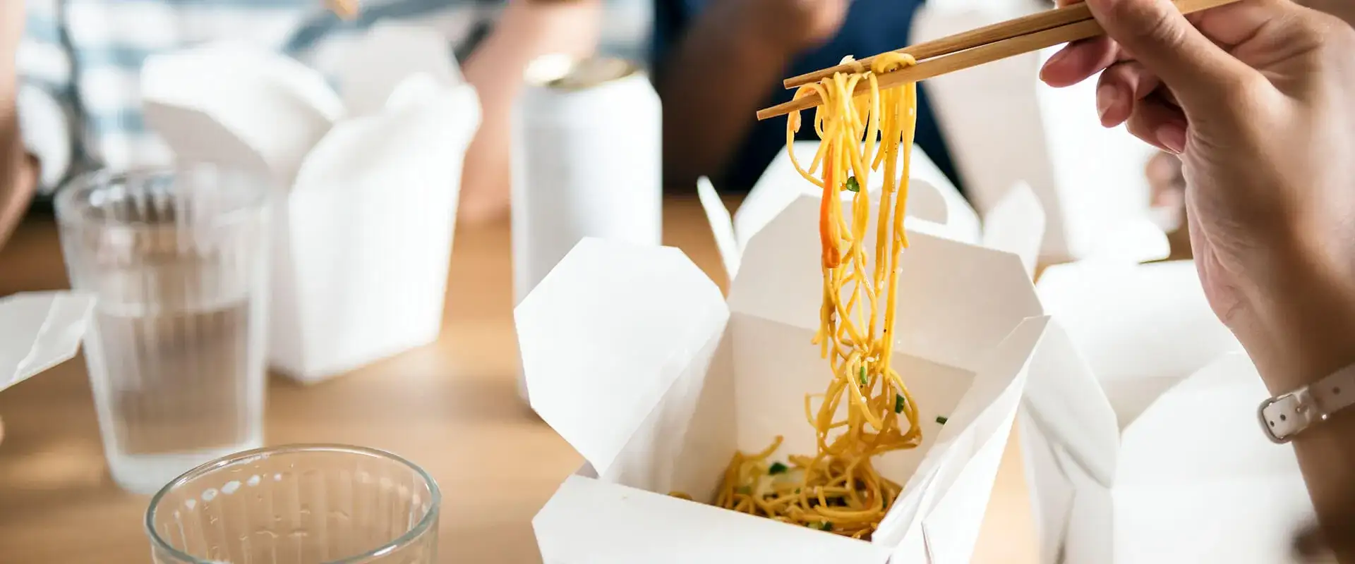 Person eating noodles from a takeout container.