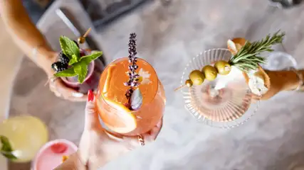 An overhead view of ladies holding 3 specialty cocktails up off the table to toast at Wolf by Vanderpump Caesars Republic Scottsdale