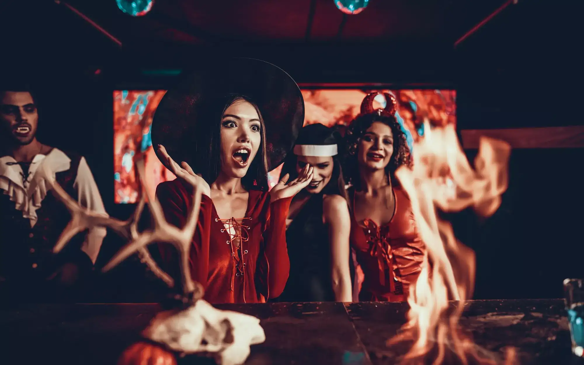 Guests in Halloween costumes gathered around a display featuring flames, antlers, and a skull