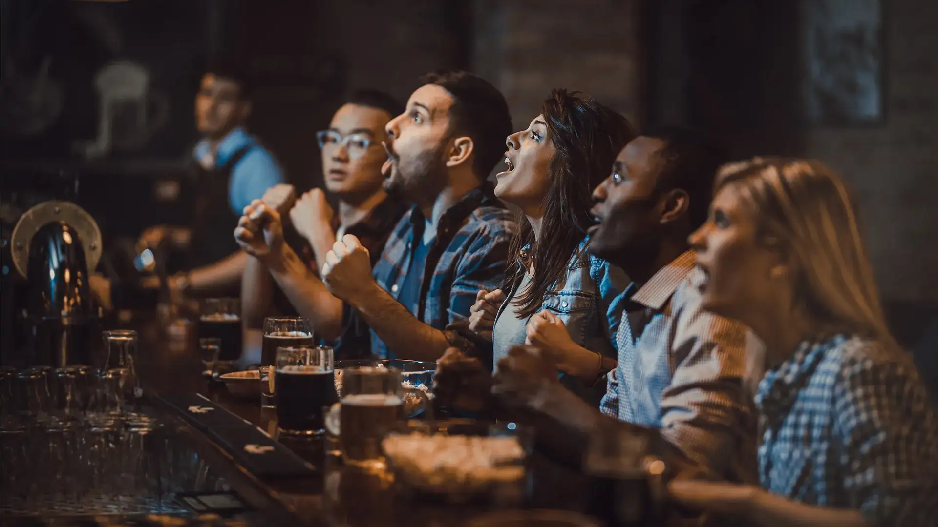 Group of men and women sitting at a bar watching a sporting event.