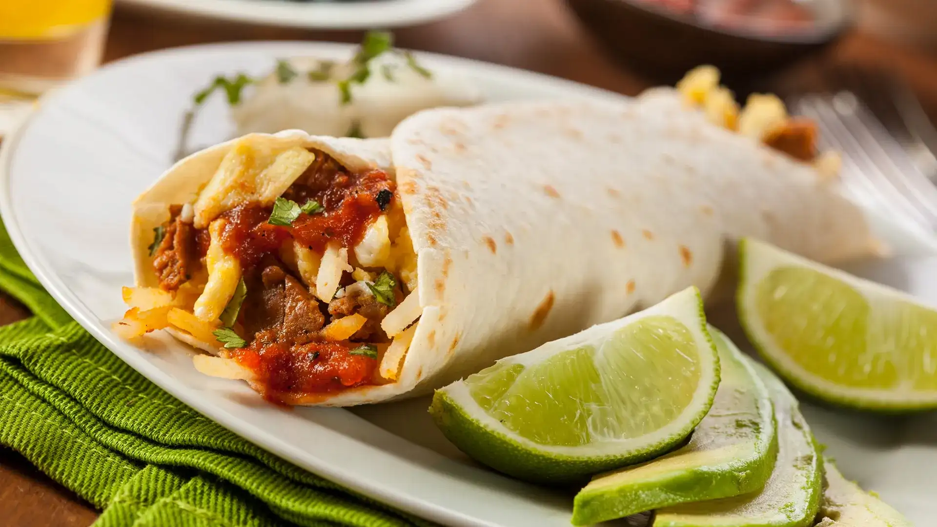 Breakfast burrito with lime wedges on the side.