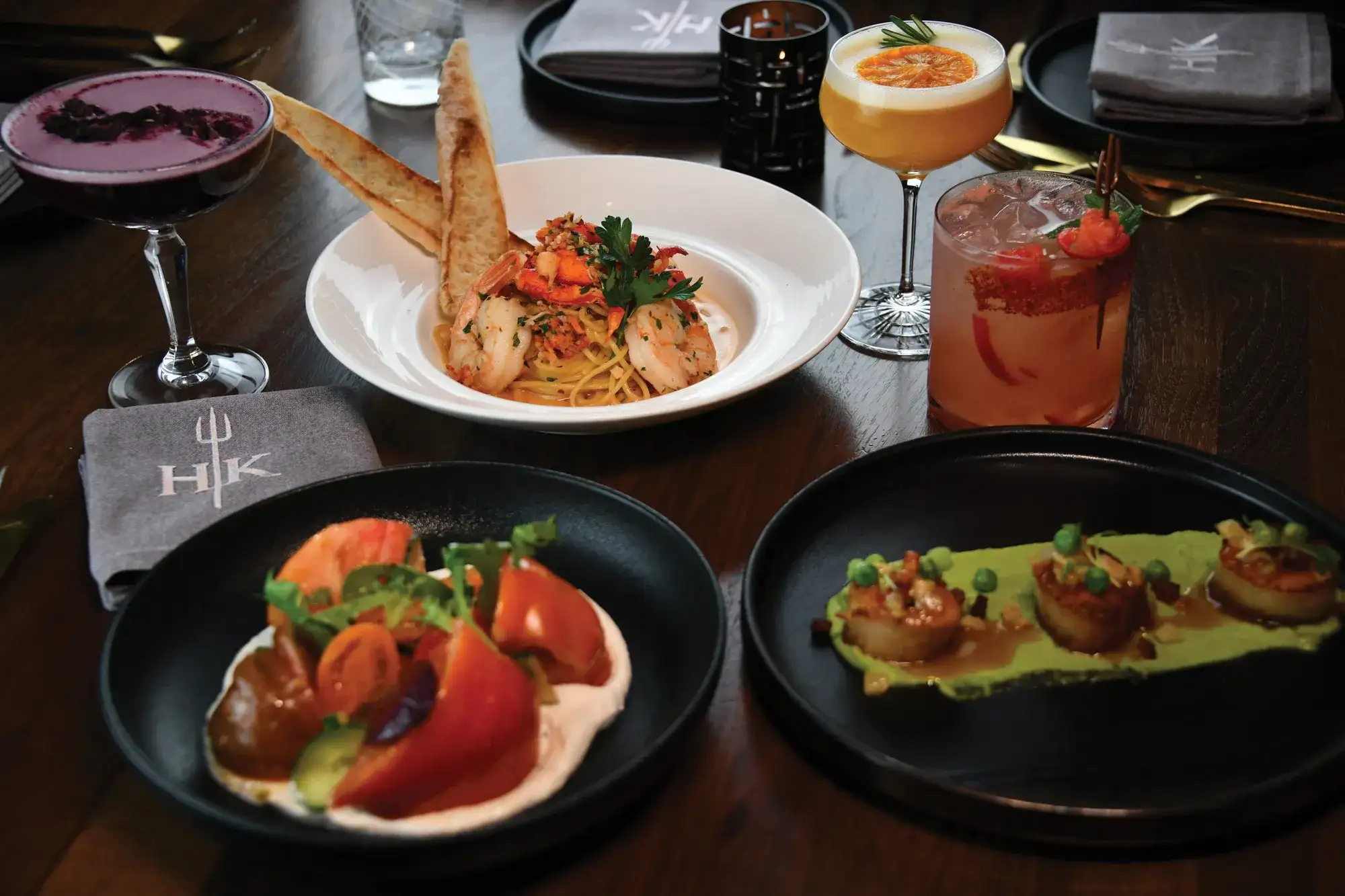 Seafood pasta, seared scallops, a tomato salad, and cocktails arranged on a table at Gordon Ramsay Hell’s Kitchen at Caesars Atlantic City