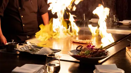 Hibachi grill with flames and food on cook surface.