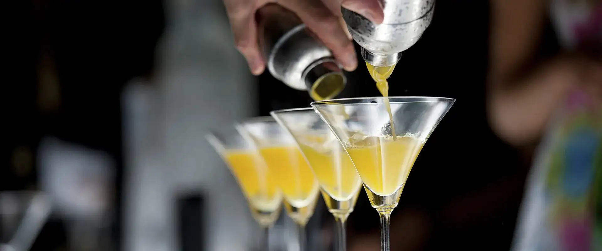 Bartender pouring cocktail in four martini glasses.