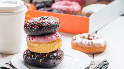 Stack of Spinkled Donuts on a plate with a drink to-go and a box of donuts.
