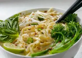 Bowl of noodles with vegetables, lime, and chopsticks