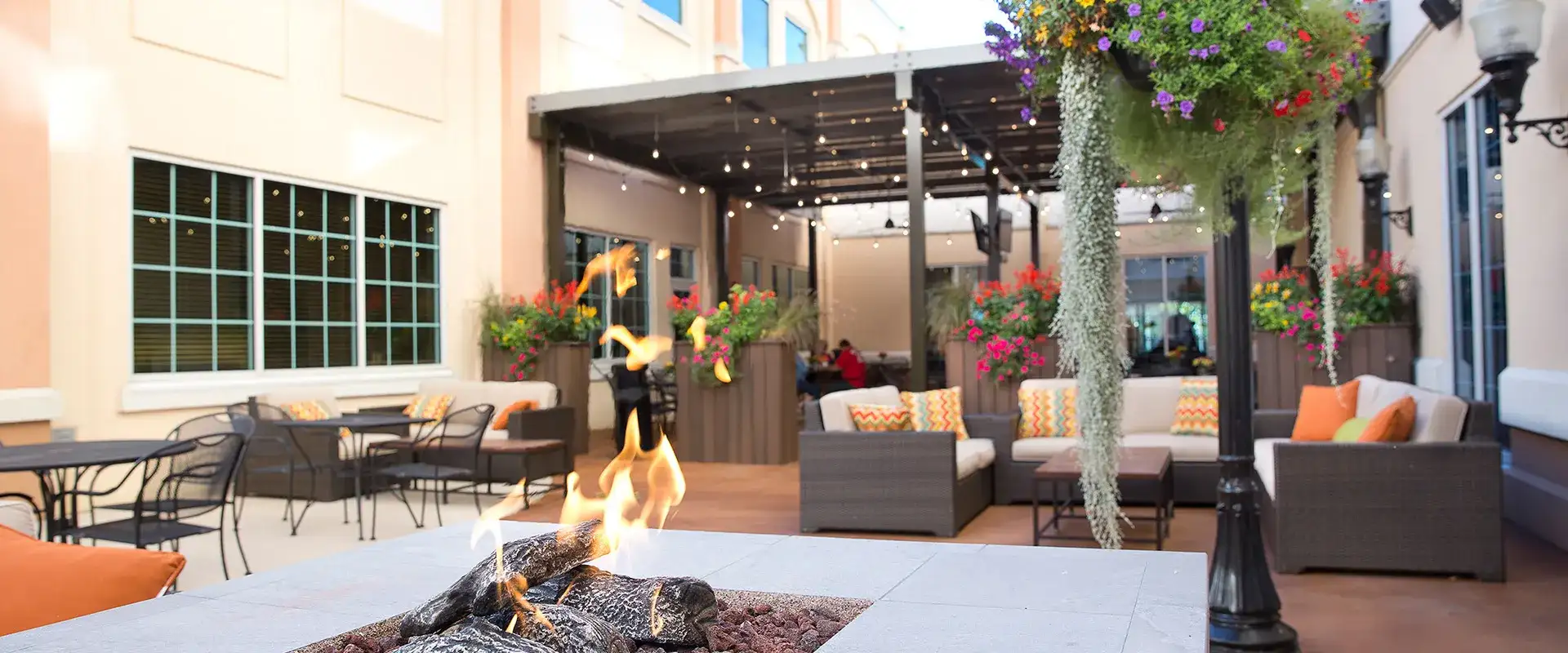 Firepit close-up with seating area and dining tables in background.