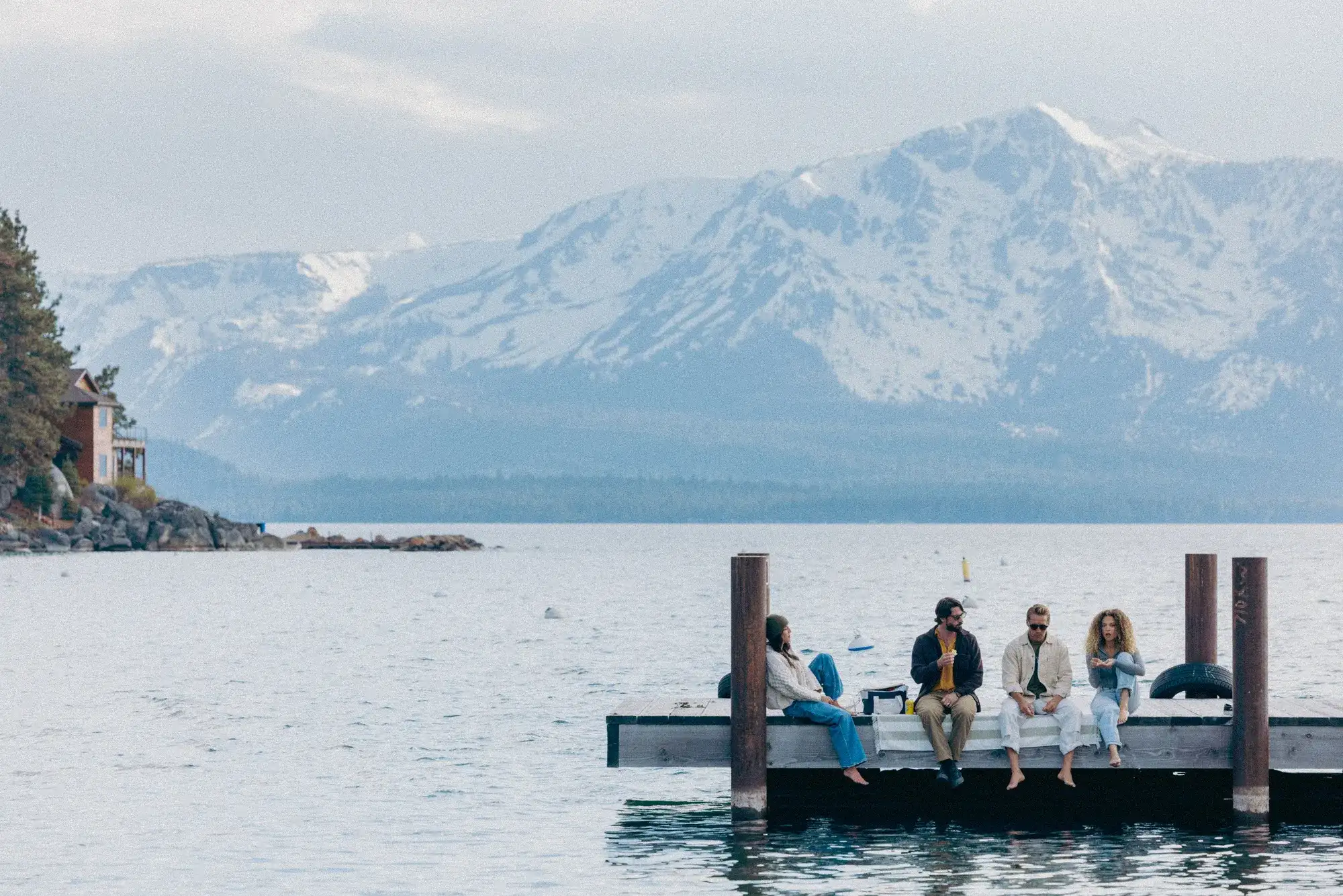 4 visitors seated on a Lake Tahoe dock beneath snow-covered Sierra mountains