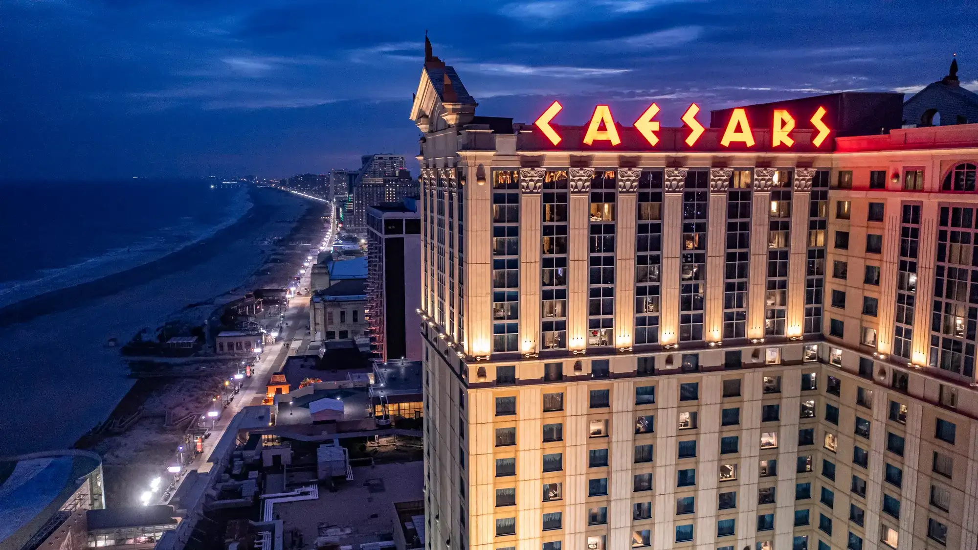 Caesars Atlantic City hotel illuminated at dusk beside the Atlantic City Boardwalk and beachfront