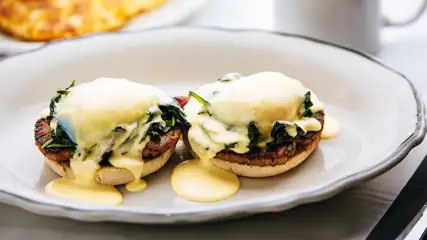 Eggs Benedict on a plate next to a drink mug.