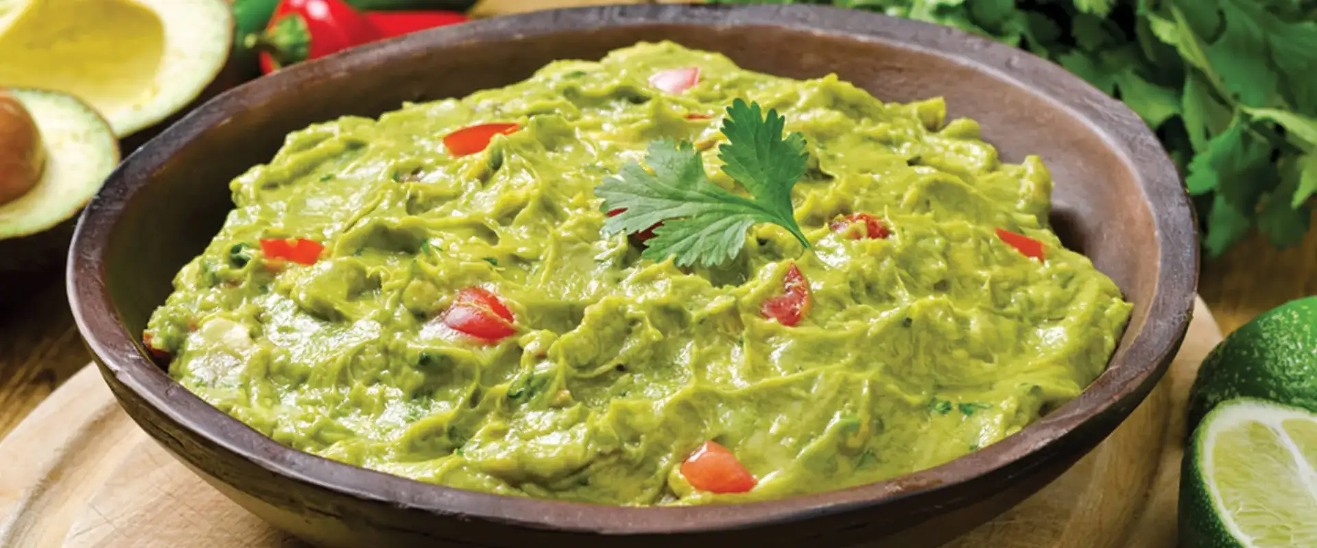 Wooden bowl with fresh guacamole and a cilantro garnish.