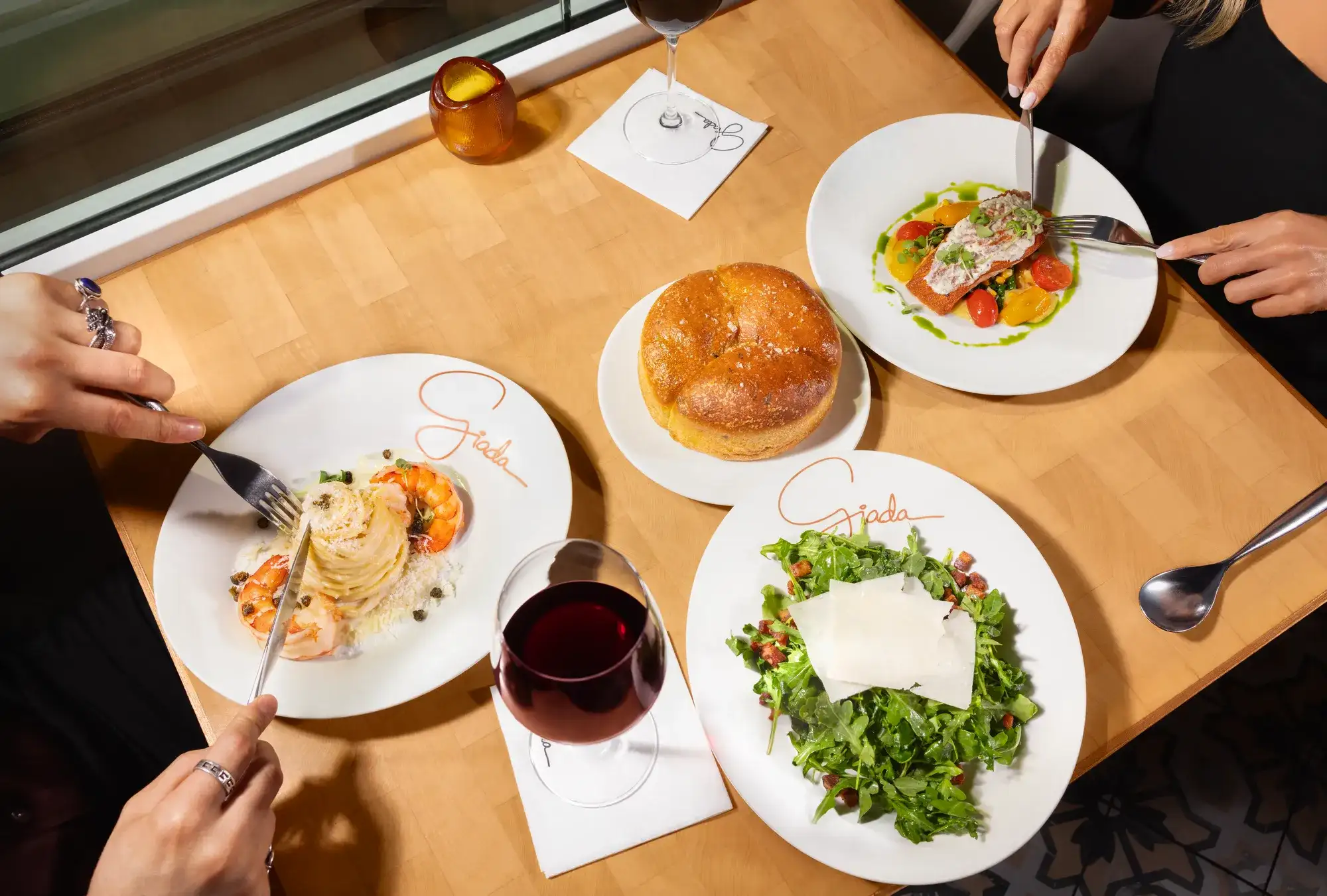 Couple celebrating with plates of food on the table at Giada at The Vanderpump Hotel