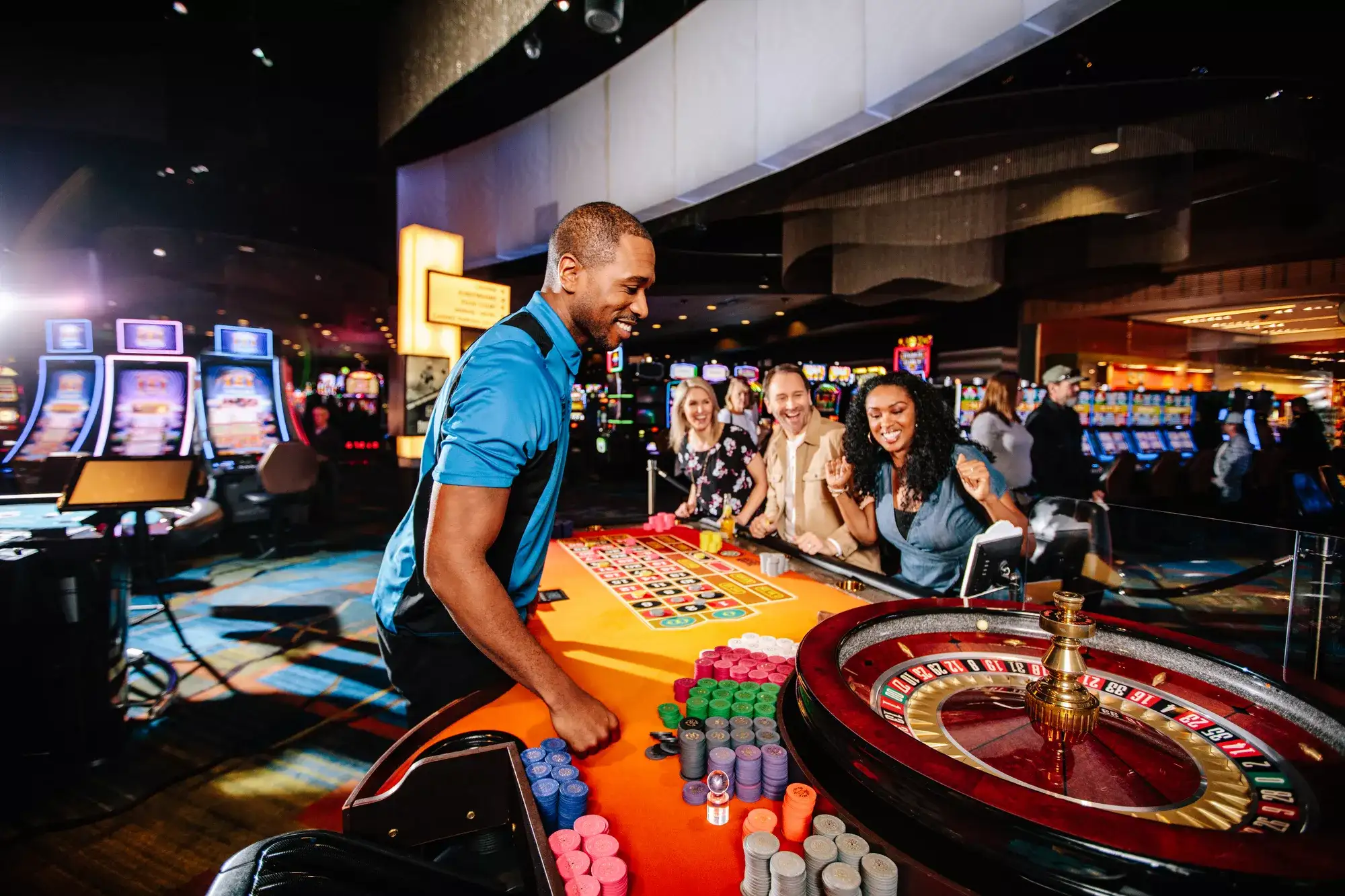 Casino guests playing roulette at a table with colorful chips, slot machines, and gaming tables in the background