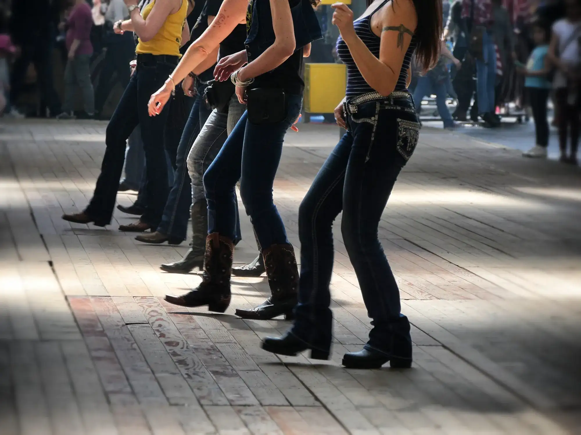 Dancers in jeans and boots performing a synchronized line dance on a wooden floor