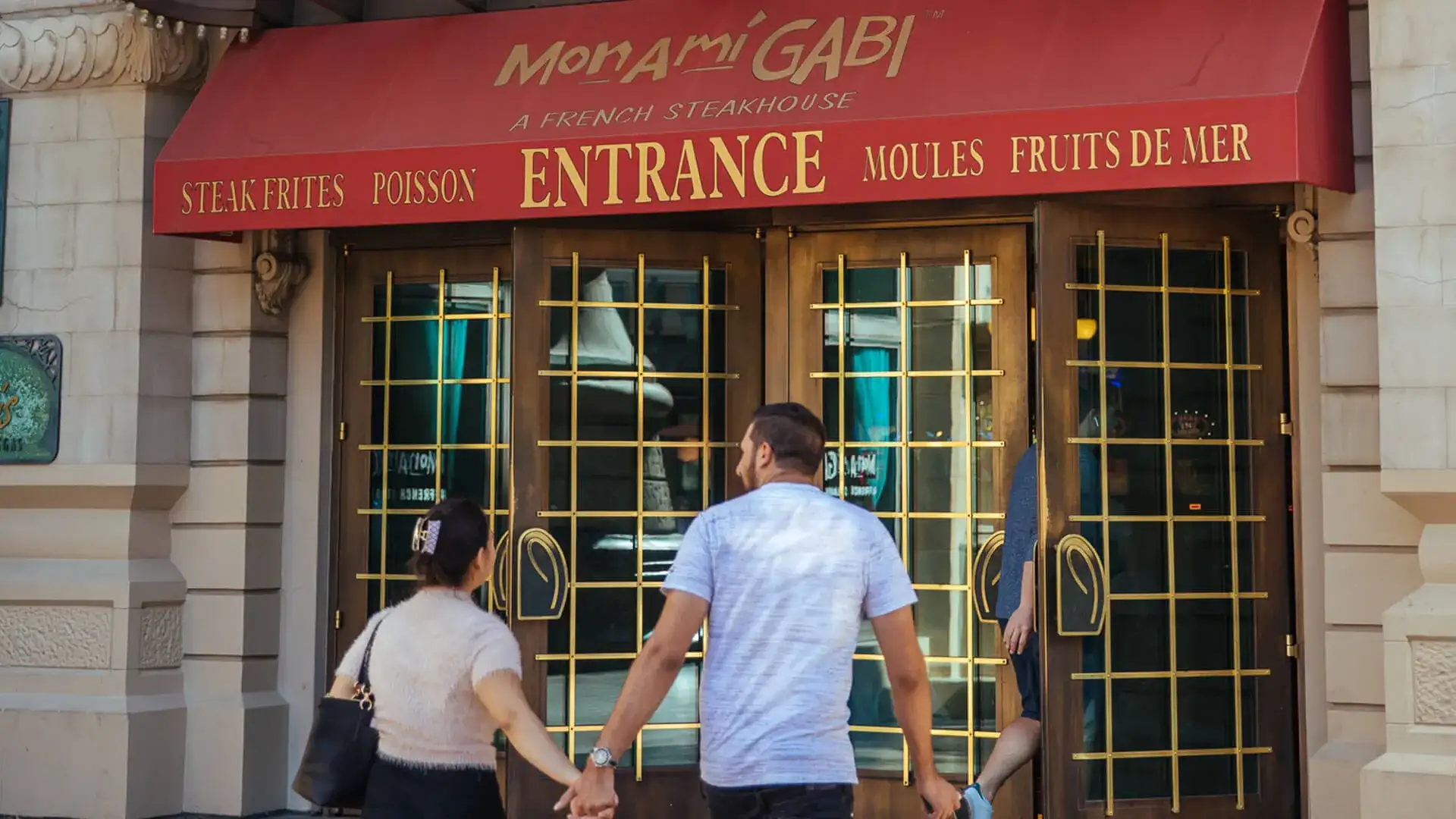 couple holding hands walking in to Mon Ami Gabi