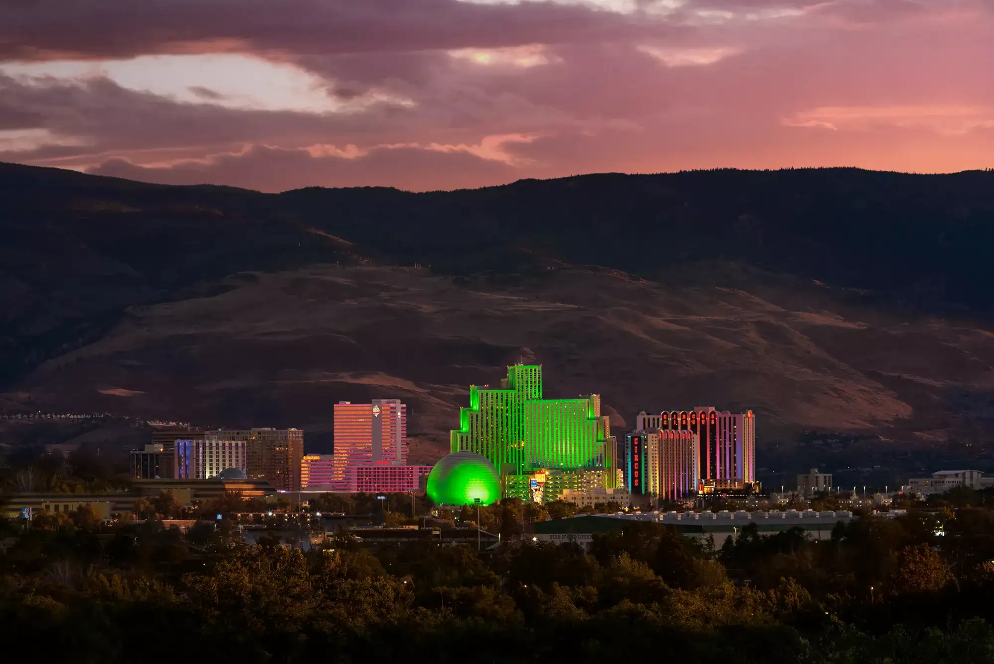 Downtown Reno skyline at sunset with casino resort towers, mountain views, and colorful evening sky