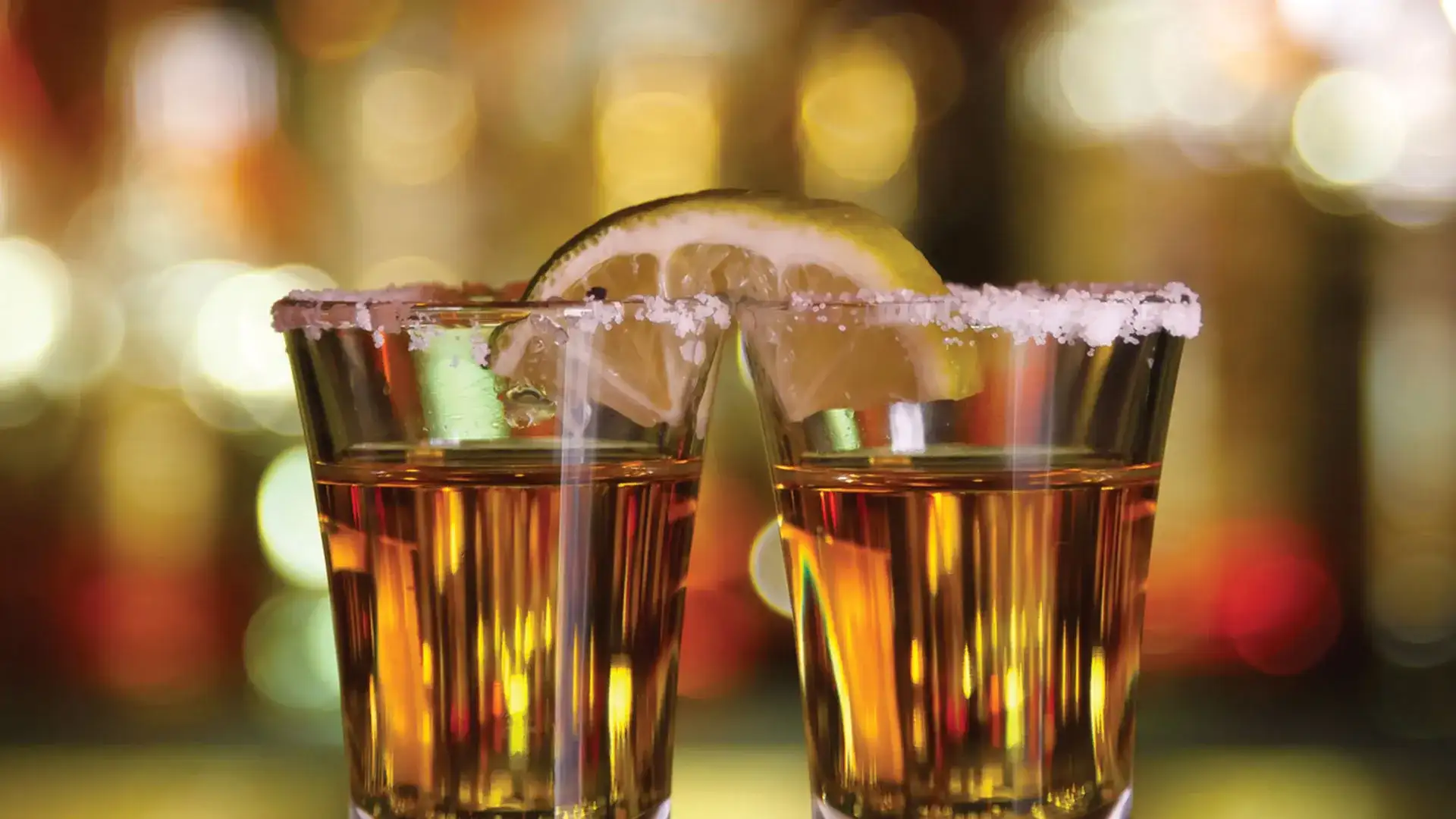 Shots of tequila with salt on the rim ad a lime wedge.