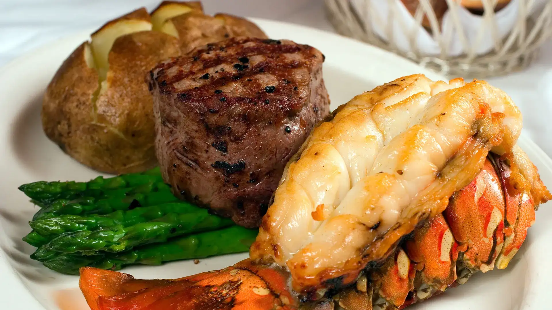Steak, lobster tail, baked potato, and asparagus.