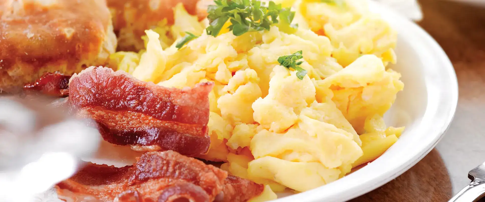 Plate of scrambled eggs, bacon and parsley garnish.