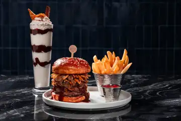 Burger plated next to fries and shake