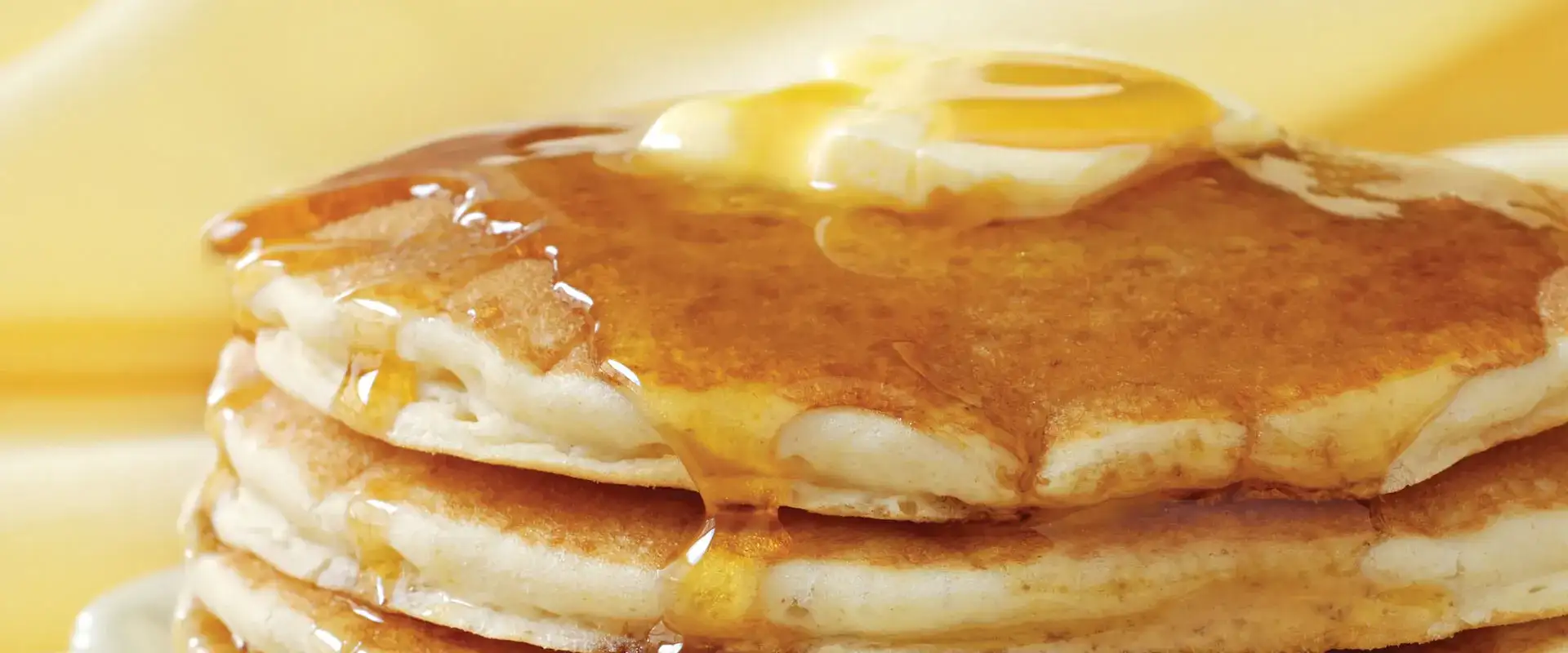 Stack of pancakes with melting butter and syrup.