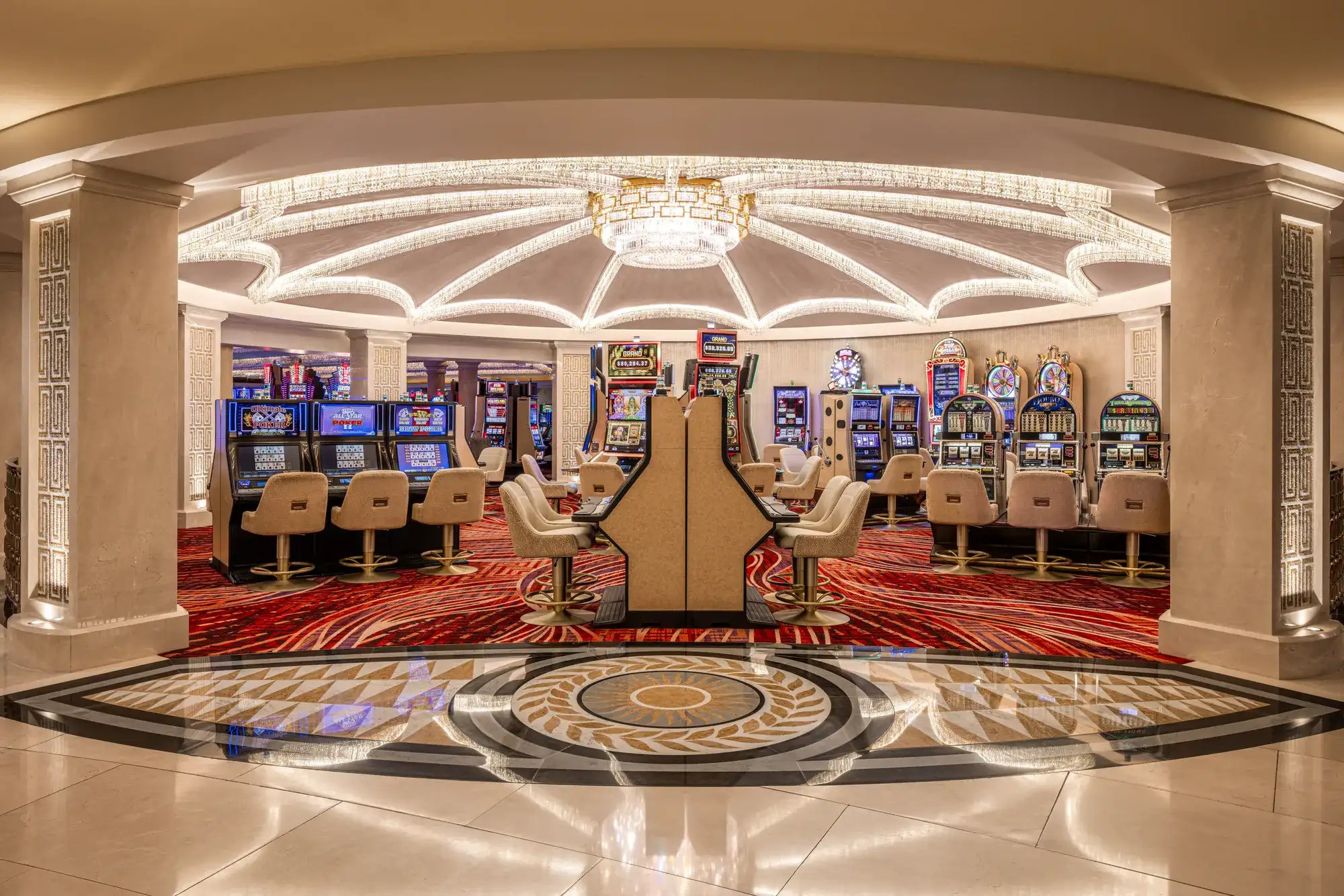Rows of slot machines and cushioned chairs on a casino floor with red carpeting and an illuminated domed ceiling