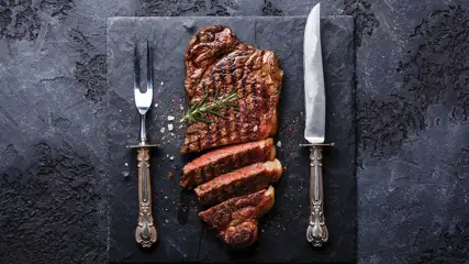 Steak on slate with fork and knife.