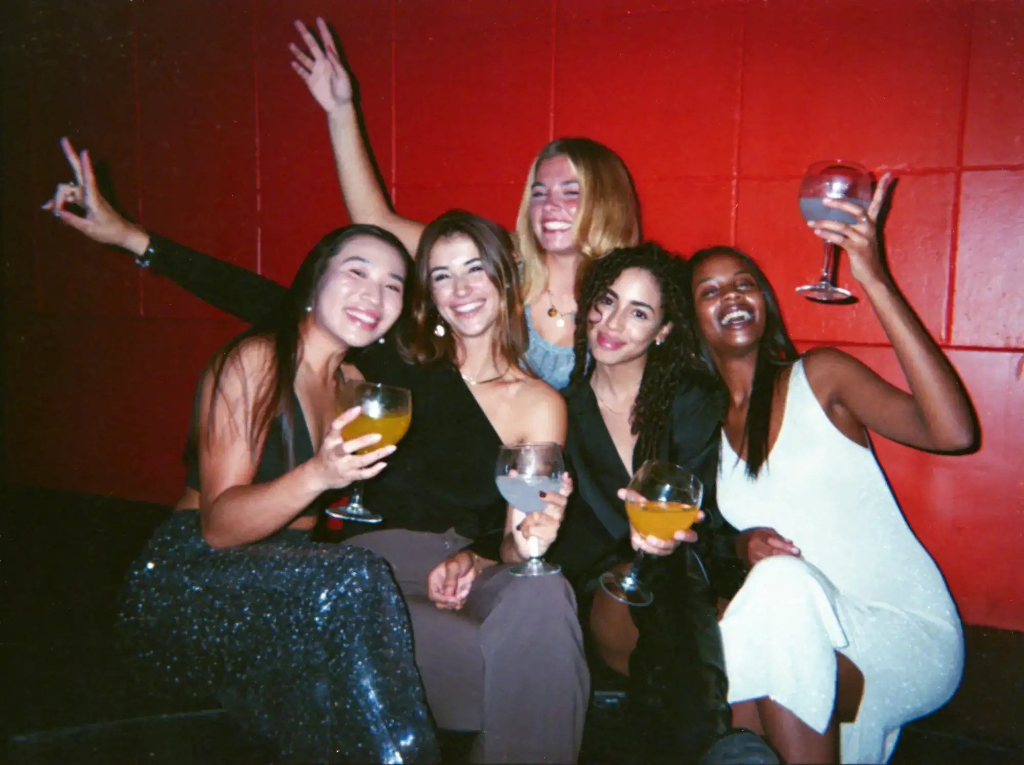 Friends posing together with cocktails in a red-walled lounge, capturing a Las Vegas girls' weekend trip moment.