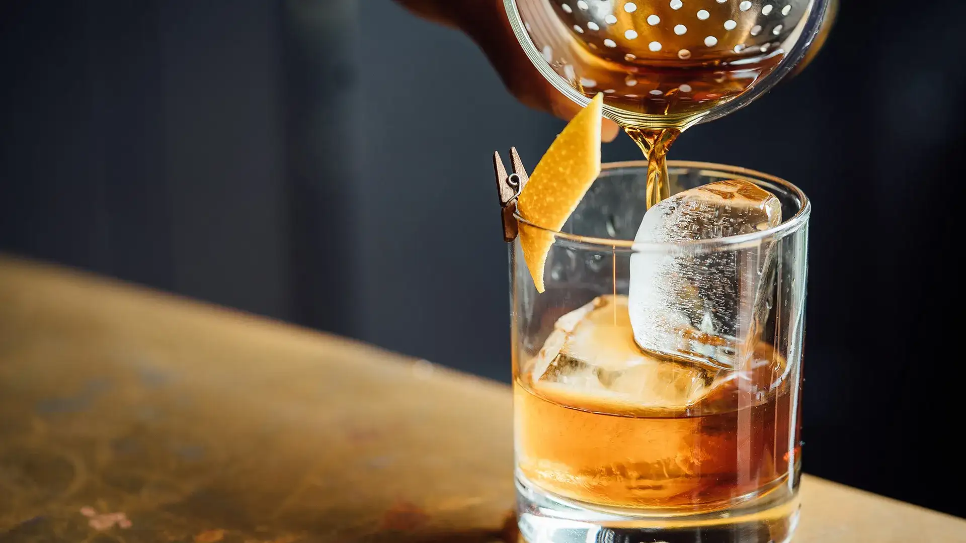 Cocktail shaker pouring cocktail into a rocks glass.