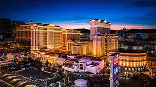 A wide-angle nighttime view of the entire Caesars Palace resort on the Las Vegas Strip, with its fountains and Roman architecture illuminated against the night sky.