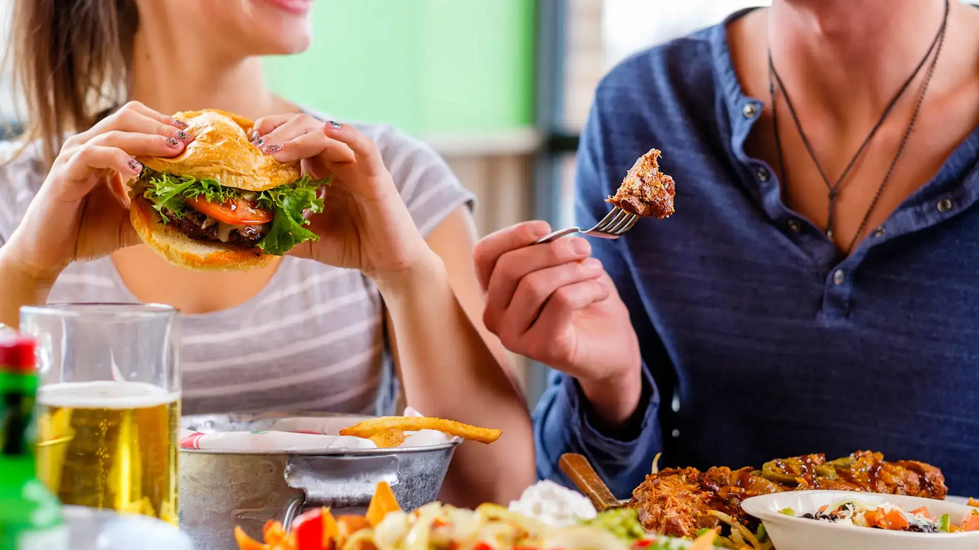 Man and woman eating a hamburger and wings.