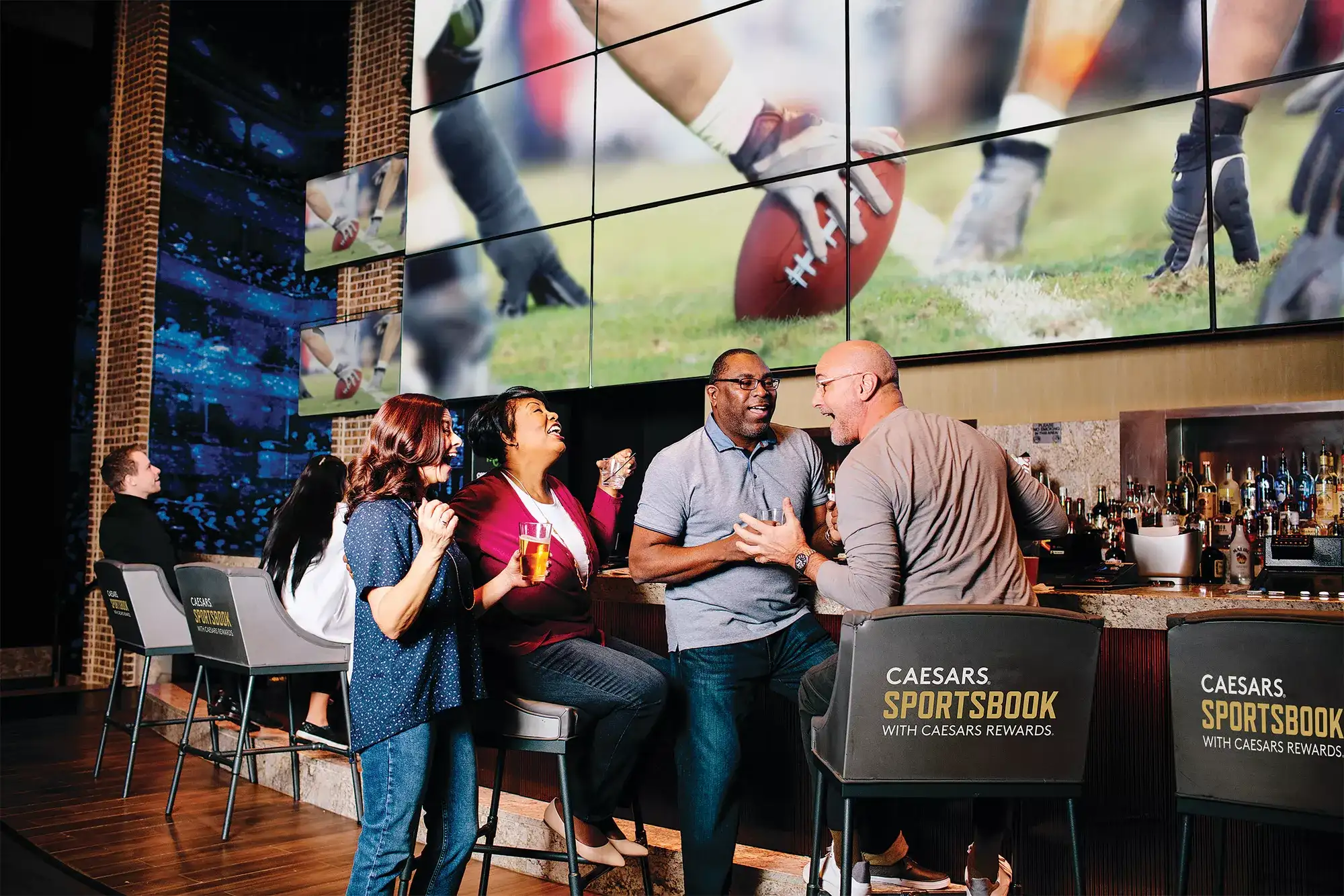 Guests seated at a Caesars Sportsbook bar watching college football on large video screens
